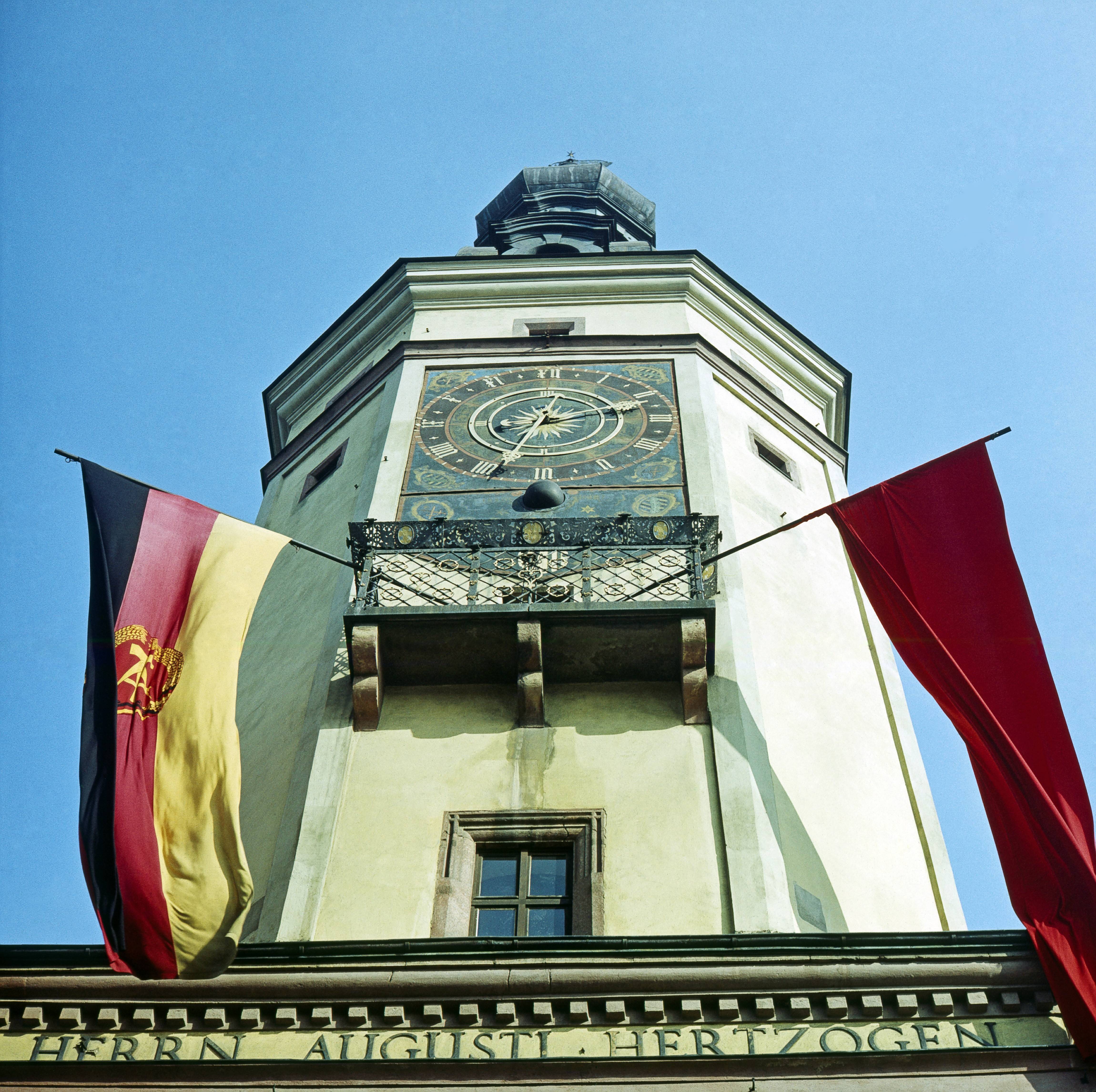 IMAGO / Harald Lange | On May Day in Germany, the GDR flag with the red workers' flag in the tower of the Old Town Hall in Leipzig. 1 May 1992, Leipzig. Labour day in Germany 90s.